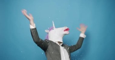 Man with unicorn mask making funny gestures. Business man with Unicorn Mask. Fun and happiness concept. Funny Guy in Gray Suits Dance with Unicorn Mask, Man having fun on isolated Blue Background. 