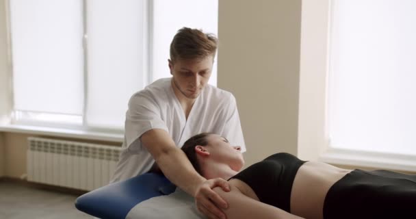 マッサージセラピストが女性の依頼人を治療する 妊娠中や授乳中の女性の首の筋肉を混練男性骨粗しょう症の手持ち撮影でズーム — ストック動画