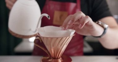 Crop man pouring water while making filter coffee. Crop unrecognizable male barista in apron filling water from kettle into cup while preparing pour over coffee in modern cafe. Barista prepares coffee