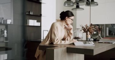 Mutfak odasında kitap okuyan genç bir kadın gözlüklü çekici bir kadın mutfak odasında eğleniyor ve boş zamanlarında el ele kitap tutuyor. Modern daire. edebiyat ve ev hayatı.