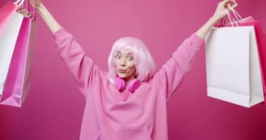 Pembe renkli çantalarla alışveriş yaptıktan sonra mutlu kız. Kadın indirimden ve yapılan alımlardan zevk alıyor. Pembe arka plan stüdyo portresi üzerinde başarılı alışveriş yaptıktan sonra gülümsüyor