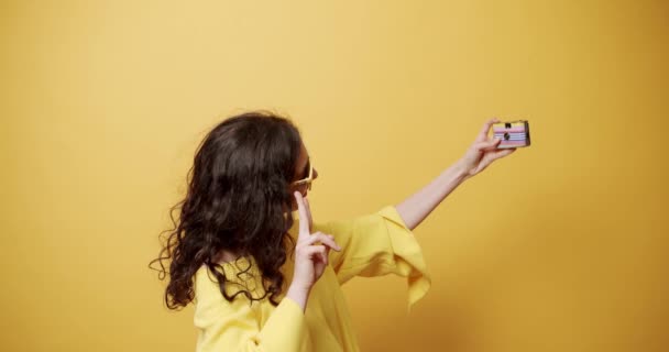 黄色の背景にレトロなカメラで写真を撮る少女は 趣味活動だ セルフ写真 メッセージをオンラインで送る 夏のリラックス ハッピー トラベル 楽しい写真 — ストック動画
