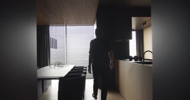 那个人穿过厨房 停在窗前 现代餐厅有木制和简约的设计 一个男人从窗户往外看 是一间有现代化厨房内部的公寓 — 图库视频影像