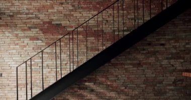 Modern bir dairede siyah merdiveni ve soyut arkaplan kompozisyonu olan eski tuğla renkli bir duvar. Sıva dokusunun delikleri ve aşınmalarla kaplanmış yüzeyi. dolly kamera hareketi.