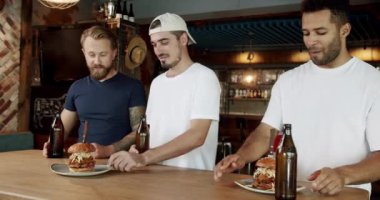 Garson müşterilere hamburger veriyor. Garsonun, bira içen ve hafta sonunu barda geçiren çeşitli mutlu adamlara lezzetli hamburgerlerle tabak dağıtırken elde çekilmiş bir fotoğrafı..
