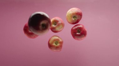 Temiz suya düşen elma. Yukarıdan, pembe arka planda, şeffaf temiz suyun ve olgun elmanın meyve yığınına düşüşünün statik görüntüsü.