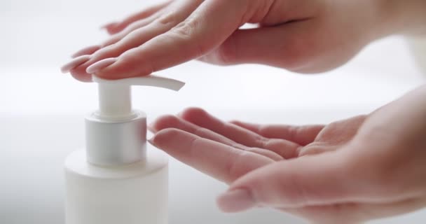 白い部屋の背景にきれいな手でクリームボトルに指を押しボタン 閉めろ 浴室での洗濯 手に保湿クリームを適用ポンププラスチック化粧水ボトルを押す女性の手 — ストック動画