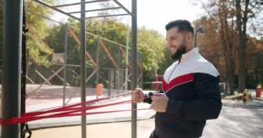 Attractive fitness man does exercising outside. Trainer male correcting fit does gym exercises with rubber band . Outdoor Athletic man does exercises with elastic band. Gym health outside concept.