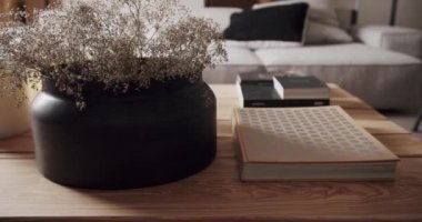 Ahşap masası, doğal çiçekleri, kitapları ve mumları olan modern oturma odası. Lüks minimalist tasarım, beyaz ve gri tonlu gerçek daire, zarif sandalye ve lüks mobilyalar..