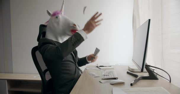 ユニコーンマスクを持つビジネスマンは 職場で現金お金ドル利益給与収入をスタック ハンサムな幸せなビジネスマンとともにユニコーンマスク円を散布 — ストック動画