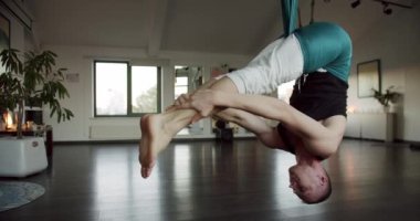 Hafif stüdyodaki yoga seansı sırasında havadan hamakta baş aşağı asılı güçlü bir erkek resmi. Yoga sınıfında kapalı alandayız. Yoga Kulübü. Konsantrasyon. Spor etkinliği.