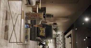 Gri mobilyaları ve tahta duvarları olan modern Minimalist oturma odası. Köşedeki kanepe, sandalye ve kitaplığı olan lüks modern ev içi. Moda mobilyalar. Ev İçi. Dikey video