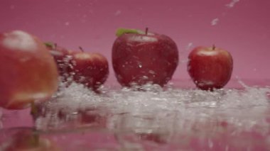 Su yüzeyinde yuvarlanan elmalar. Bütün kırmızı elmaları yüzeye yuvarlarken, kırmızı elmalara ve yumuşak ışıkta pembe arkaplana su sıçratırken statik görüntü.