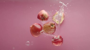Temiz suya düşen elma. Yukarıdan, pembe arka planda, şeffaf temiz suyun ve olgun elmanın meyve yığınına düşüşünün statik görüntüsü.