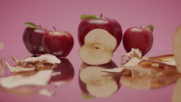 新鮮で乾燥したリンゴチップを積層します スタジオピンクの背景の脇に全体の赤いリンゴと鏡面上のリンゴの乾燥した山と生のジューシーなスライスをクラッシュの静的なショット — ストック動画