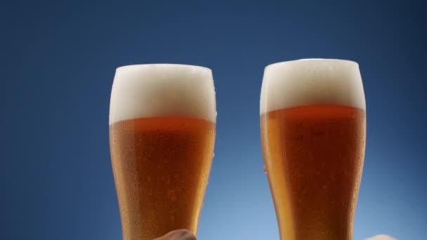 Dos Vasos Llenos Cerveza Espumosa Chocan Medio Sobre Fondo Azul — Vídeo de stock