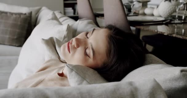 年轻女子平静地度过了一个健康的白天 舒适地躺在沙发上 眼睛紧闭 双手紧握着头 安详地睡在床上 呼吸着新鲜空气 靠着舒适的沙发躺在现代的家里 — 图库视频影像