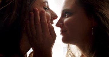 Kızlar birbirlerinin gözlerinin içine bakar ve güzelce gülümserler. Tatlı öpücük. Yüze yakından bak. Gözlerinin içine bak. Lgbt ve lezbiyen kadınlar evde. Sarılın ve birbirinize sarılın..
