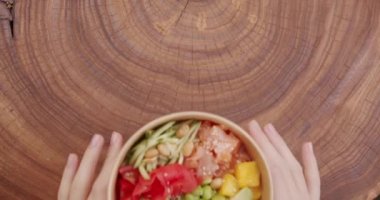 Poke bowl with salmon, rice, avocado, edamame beans, cucumber on a wooden background. Poke bowl, traditional Hawaiian raw fish salad. Organic and clean eating. Fresh fish and vegetables on diet lunch.