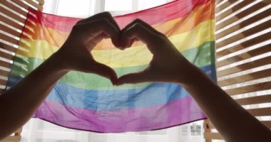 Destekleyen eller kalp işareti yapar ve gökkuşağı bayrağının önünde dalgalanır. Gay ve lezbiyen gururu Igbt bayrağı. Aşk işareti. LGBT 'nin kutlama etkinliği sembolü. Aşk Eşitliği. LGBT hakları. İnsan ilişkileri.