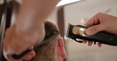 Yakışıklı adam elektrikli budayıcı ile yeni bir saç stili alıyor. Makyaj işiyle kapat. Modern berber dükkanında sakal ve bıyık bakımında genç hippi beyaz adam. Erkek saç stili. 