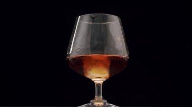 Luxury brandy. Glass with golden cognac on isolated black background with ice cube. Brandy, cognac, and whisky. Slow motion. Luxury Drink Whisky with smoke. The ice falls into the whiskey glass.