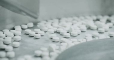İlaç fabrikasının atölyesinde metal otomatikler üzerinde hareket eden beyaz haplar. Hap ve uyuşturucu üretimi süreci. Fabrika ekipmanı ve makine taşıyıcısı. Endüstriyel ilaç konsepti.