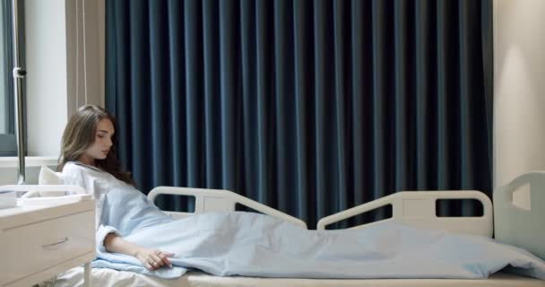 潘在医院的轻病房里 看到一个黑头发的年轻病人舒服地躺在靠窗的床上 住院病房卧床女病人年轻的女病人躺在医院房间里 — 图库视频影像