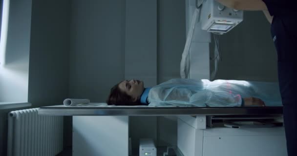 X光机上的女性病人在现代实验室的腹部X光扫描过程中 左右两方面都可以看到穿着一次性长袍的女性躺在桌子上 医院放射科室 — 图库视频影像