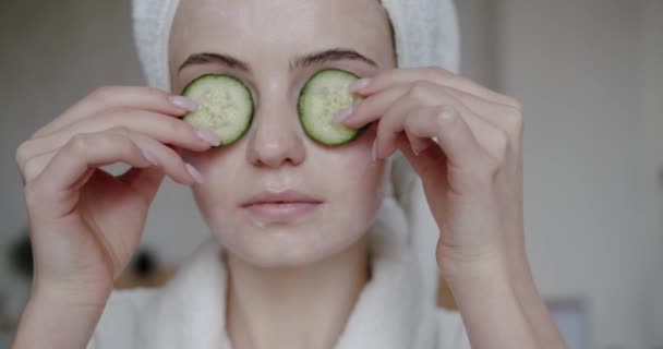新鮮なきれいな健康的なスキンケアの概念を宣伝キュウリで目をカバー彼女の頭の上にタオル付きバスローブで面白い幸せな若い女性 水分補給と保湿のコンセプト アンチエイジング — ストック動画