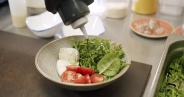 Yeşil yapraklar, beyaz arka planda beyaz bir tabakta ıspanak. Vejetaryen yemekleri, organik yiyecekler. Lezzetli salata. Yemek pişirmek. Ağır çekim. Malzemeler. Lezzetli salata. Çeri domates, roka ve mozzarella..