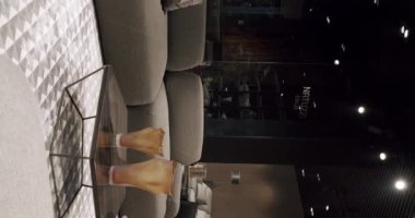 Gri mobilyalı modern Minimalist oturma odası. Köşedeki kanepe, sandalye ve kitaplığı olan lüks modern ev içi. Lüks Zarif Oda. Gayrimenkul özel evi. Dikey video.