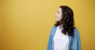 Happy young female with curly brown hair holding bank card and looking amazed with great credit provision showing thumb up on yellow background. Smiling woman promoting credit card. 