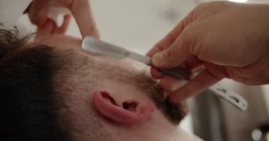 Berber dükkanında eski moda bıçakla kesilmiş bir sakal. Yakışıklı adamın sakalını kuaförde traş ettiriyor. Sakalını kesiyor. Profesyonel berber, müşteri sakalını ustura ile tıraş eder.. 