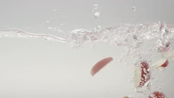 掉进干净的水里的苹果楔子 白色底色透明清澈水慢动作静态拍摄及落叶成熟红苹果片 — 图库视频影像