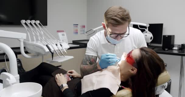 歯科現代のクリニックで患者のための歯の洗浄を行う歯科医 現代の歯科医院 歯科での衛生歯の洗浄手順で女性患者 歯クリーニング 超音波スケーリング — ストック動画