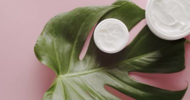 Doğal malzemelere dayalı kozmetik yağları, fırça, tonik, vücut bakımı. Pembe arka planda kozmetik ürünleri için tropikal yapraklı şişe bakım kremi. Organik kozmetik ürünleri. Üst görünüm.