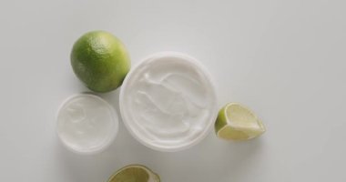 Kozmetik ürünleri için ıhlamur meyveli beyaz kavanozlar ve tüpler stüdyoda beyaz bir arkaplanda dönüyor. Doğal malzemelere dayalı kozmetik yağları, fırça, tonik, vücut bakımı. Doğal kozmetik cilt bakımı.