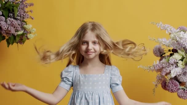7歳の少女は明るいブルーのドレスを着ており スタジオの黄色の背景の部屋を美しく見ています 小さなブロンドかわいい女の子の顔 — ストック動画