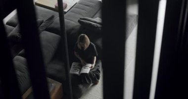 A woman is sitting on the couch and reading a book. Modern contemporary Minimalist living room with white wall and black furniture. Luxury Modern House Interior With Corner Sofa and Bookshelf.