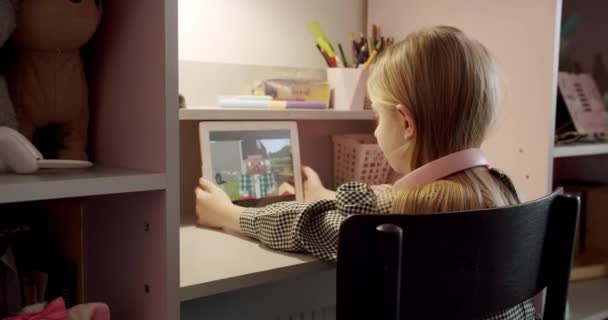 7歳の女の子は ピンクのヘッドフォンとデジタルコンピュータタブレットを使用して子供部屋で遊んでいる ソーシャルネットワークでクールなビデオや写真のコンテンツを楽しんで オンラインゲームをプレイしている — ストック動画