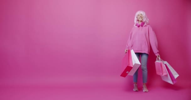 ピンク色のコンセプトでカラフルなバッグで買い物した後のハッピーガール 女性は割引と行われた購入を楽しんでいます ピンクの背景のスタジオのポートレートに隔離された成功した買い物の後 — ストック動画