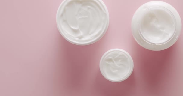 トップビュースキンケアクリームとホワイトボトルは スタジオでピンクの背景に化粧品のために回転します 天然成分に基づく化粧品油 スクラブ 強壮剤 ボディケア 異なる化粧品ボトルのグループ — ストック動画