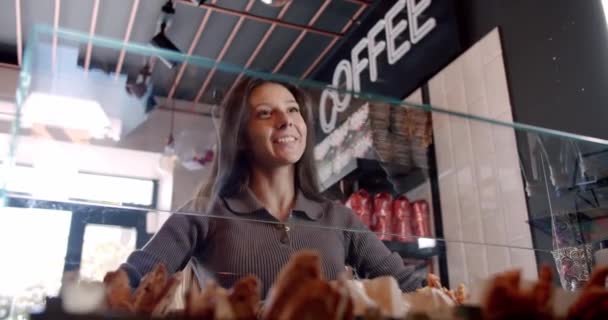 在现代咖啡店里 有识之士的年轻女性顾客 有着长长的黑发 斜视着 微笑着 一边选择咖啡 一边与无法辨认的咖啡店老板交流 — 图库视频影像