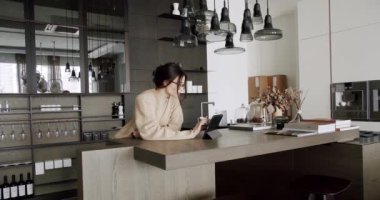 Beautiful woman at home using digital tablet in modern kitchen room and loft apartment. ooking digital tablet for follow news, work and social media online in loft kitchen at home