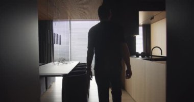 Bir adam pencereden modern mutfağı olan bir daireye bakar, adam mutfaktan geçer ve pencerenin önünde durur. Ahşap ve minimalist tasarımı olan modern yemek odası..