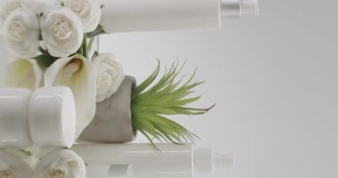 Beyaz şişe ve kozmetik için çiçekli tüpler stüdyoda beyaz bir arka planda. Doğal malzemelere dayalı kozmetik yağları, fırça, tonik, vücut bakımı. Hikayeler için dikey video.