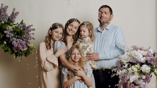 スタジオの花と白い背景の内側の写真のために立っている家族の肖像画 子供たちと一緒に幸せな若い家族 フレンドリーな家族の概念 — ストック動画