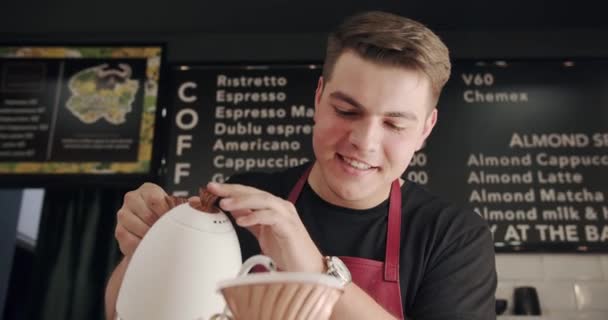 エプロンの男性バリスタは 現代のカフェでコーヒーを注ぐ準備しながら ケトルからカップに水を充填します 専門のコーヒーショップでラテアートを作るバリスタ — ストック動画