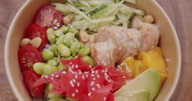 Poke kasesi, geleneksel Hawaii çiğ balık salatası. Organik ve temiz yemek. Karides, pirinç, avokado, mango, edamame fasulyesi, ahşap zemin üzerinde salatalık. Sağlıklı yemek, keto diyeti konsepti.